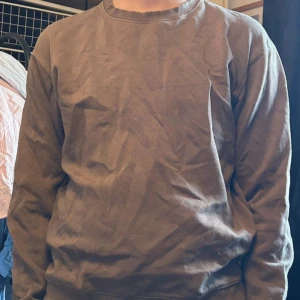 Brun sweatshirt från Jack and Jones - En enkel brun sweatshirt med rund hals och långa ärmar. Tröjan har en klassisk passform och är tillverkad i mjuk bomull, perfekt för chill dagar. Inga synliga detaljer eller mönster, bara clean och basic stil.