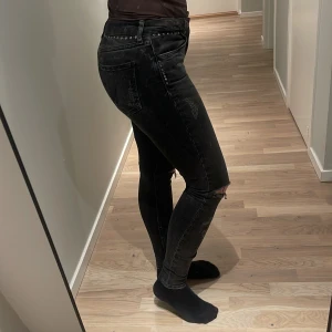 Svarta skinny jeans från Zara Woman - Snygga svarta jeans från Zara Woman Premium Denim Collection med skinny passform och hög midja. Jeansen har slitningar vid knäna, silverfärgade nitar längs fickorna och klassisk femficksdesign. Perfekta för dig som gillar en edgy stil.