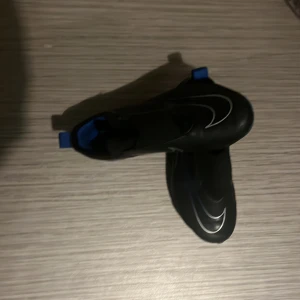 Nike svarta fotbollsskor med blå detaljer - Säljer ett par svarta Nike fotbollsskor med blå sula och blå detaljer. Skorna har en stilren design med vit Nike-logga på sidan och ovansidan. Perfekta för dig som vill sticka ut på planen med snygg och sportig look.