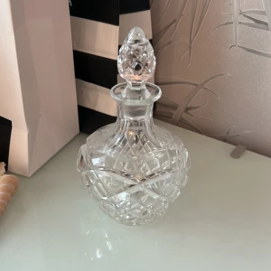 En glasprydnad - Snygg kristallflaska för parfym eller doftolja. Perfekt som dekorativt inslag på sminkbordet eller för dig som vill ha en unik behållare till din favoritdoft. Flaskan är tom och har ett elegant mönster. Volym och ursprung ej angivet.