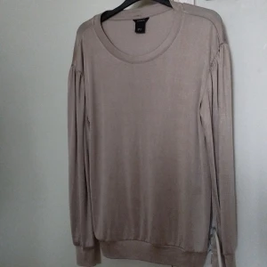 Beige långärmad tröja från Lindex - Säljer en beige långärmad tröja från Lindex i storlek M. Tröjan har rund halsringning, lätt puffade axlar och är tillverkad i ett mjukt, tunt material som känns skönt mot huden. Perfekt för lager-på-lager under hösten eller våren.
