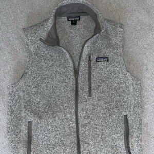 Grå fleeceväst från Patagonia - Säljer en gråmelerad fleeceväst från Patagonia med hög krage och hel dragkedja. Västen har tre fickor med dragkedja och ett diskret Patagonia-märke på bröstet. Helt fräsch med inga defekter alls.