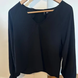 Svart blus med v-ringning Vero Moda - Svart blus från Vero Moda i storlek S. Blusen har en snygg v-ringad hals och långa ärmar. Enkel och stilren design som funkar till många olika looks. Materialet känns lätt och bekvämt mot huden.