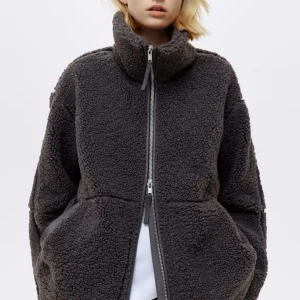Mörkgrå teddyjacka med dragkedja - Säljer en mörkgrå teddyjacka med hög krage och grov dragkedja framtill. Jackan har en oversized passform och är tillverkad i mjuk fleece som ger en riktigt mysig vibe. Perfekt för kalla dagar när du vill vara både chill och varm.