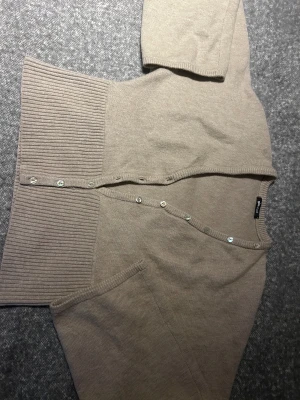 Beige kofta från Gina Tricot XL - Snygg beige kofta från Gina Tricot i storlek XL. Koftan har ribbade partier vid nederkant och ärmslut, samt pärlemorsknappar framtill. Materialet är mjukt och stickat, perfekt för lager på lager. Enkel och clean design som funkar till många stilar.