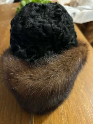  pälsmössa med brun kant - Snygg och klassisk svart mössa med fluffig brun päls runt kanten. Mössan har en rund form och är tillverkad i pälsmaterial som ger en lyxig och varm känsla. Perfekt för kalla vinterdagar när du vill sticka ut med en unik accessoar.