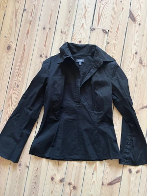 Skjorta från Mexx - Svart skjorta från Mexx med schysst krage och coola knappar på ärmarna. Skjortan är rätt tight men finns en dragkedja på sidan. Det står att det är en L men skulle säga att den skulle sitta perfekt  som en M eller tom S om man vill ha lite lösare fit! 