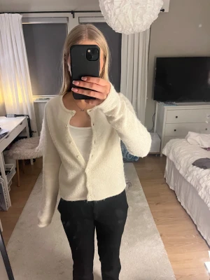 Vit fluffig kofta med knappar - Supermysig vit kofta med rund hals och knappar hela vägen framtill. Den är fluffig och har långärmade ärmar.