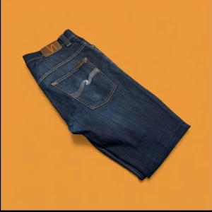 Nudie Jeans - Nudie Jeans – Stilrent och hållbart denimval  Säljer ett par mörkblå Nudie Jeans i utmärkt skick. Dessa jeans är tillverkade av högkvalitativ, ekologisk bomull, vilket gör dem både sköna och slitstarka. Nudie Jeans är kända för sin tidlösa design och sitt engagemang för hållbarhet.  *   Material: 100% ekologisk bomull *   Färg: Mörkblå *   Skick: Utmärkt, väl omhändertagna.