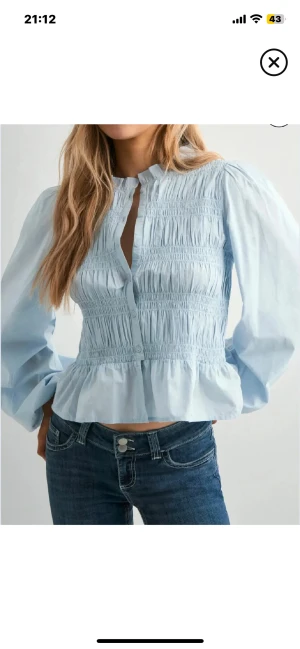 Ljusblå blus med smock och puffärm - Säljer en ljusblå blus med smockad front och knappar. Blusen har puffiga långärmar och en lätt volang nedtill som ger en söt och trendig look. Perfekt att styla med jeans eller kjol för en fräsch vibe. PRISLAPP KVAR