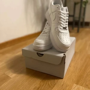 Nike Air Force 1 '07  - Fräscha Nike Air Force 1 '07 sneakers i helvit färg med klassisk design och rund tå. Skorna har snörning, platt sula och är tillverkade i skinn med perforerade detaljer på tån för extra ventilation. Perfekt för dig som gillar stilrena och tidlösa sneakers.