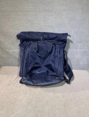 Svart ryggsäck från Nike med quiltad rygg - Snygg svart ryggsäck från Nike med stilren design och quiltad ryggpanel. Väskan har ett stort huvudfack med dragkedja, praktiska innerfickor och justerbara axelremmar. Perfekt för dig som vill ha en sportig och funktionell väska med klassisk Nike-logga framtill.