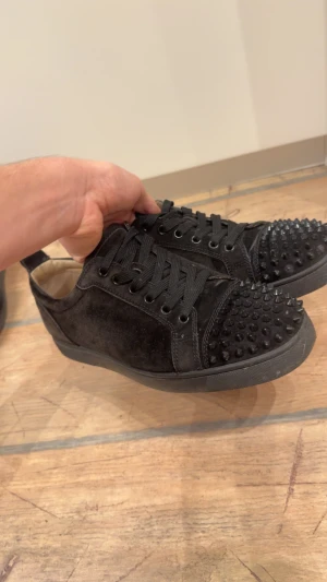 Svarta sneakers med nitar från Louboutin - ✅KVITTO FINNS✅Säljer ett par svarta sneakers från Christian Louboutin med coola svarta nitar på tån och klassisk röd sula. Skorna har snörning och är gjorda i mocka med detaljer i skinn. Perfekt för dig som gillar edgy stil och vill sticka ut.