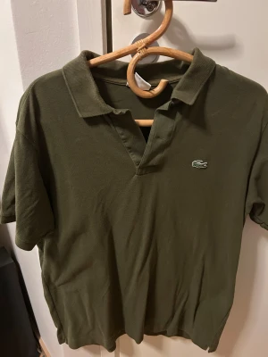 Olivgrön pikétröja från Lacoste - Snygg olivgrön pikétröja från Lacoste. Storlek är 4 o fittar som M. Skjortan har inge fel, och är i utmärkt konditon.