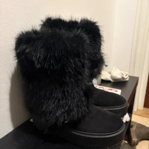 NYA Svarta pälsboots från Bershka  - (köpte skorna idag och ångrade mig och fick inte lämna tillbaka dem då kassörskan hade klippt bort lappen) Säljer ett par svarta boots från Bershka i storlek 39. De har fluffig konstpäls upptill, mockaliknande material på foten och en platt sula. Bootsens design är chunky och har en silverfärgad spänndetalj på sidan. Perfekta för kalla dagar med extra stil.