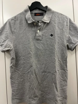 Grå pikétröja Morris S - Snygg grå pikétröja från Morris i storlek S. Klassisk krage, korta ärmar och två knappar framtill. Diskret broderad logga på bröstet. Mjuk bomullskvalitet som känns skön mot huden. Perfekt för en clean och stilren look.