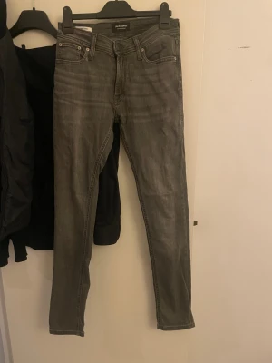 Grå skinny jeans från Jack & Jones - Säljer ett par gråa skinny jeans från Jack & Jones med klassisk femficksdesign och dragkedja. Jeansen har en smal passform och är tillverkade i stretchig bomull för extra komfort. Perfekt för dig som gillar en modern och stilren look.