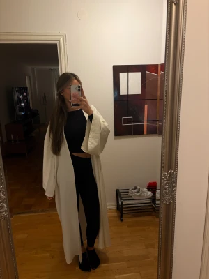 Vit lång kappa med vida ärmar - Säljer en vit, superlång kimono med riktigt schyssta vida ärmar. Den har en clean och minimalistisk look, utan synliga knappar eller dragkedja. Perfekt för dig som gillar oversized vibes och vill sticka ut med en enkel men stilren.