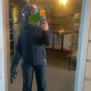 Svart Peak performance jacka med dragkedja - Säljer en svart vinterjacka med dragkedja och hög krage. Perfekt för kalla dagar. Jackan har en stilren design och är idealisk för vintersäsongen. Dragkedjan krånglar