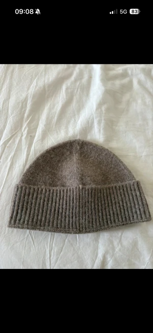 Beige ribbstickad mössa från Calliope - Snygg beige mössa från Calliope i mjuk ullblandning. Klassisk modell med bred ribbstickad uppvikning som ger en clean och stilren look. Perfekt för kyliga dagar när du vill hålla värmen och ändå se fräsch ut.