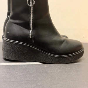 Svarta boots med platå och dragkedja - Säljer ett par svarta boots med platåsula och rund tå. Skorna har dragkedja på sidan och är fodrade med mjukt material på insidan. Hur mycket jag än vill så trivs jag inte i skorna. Dom är använda ett fåtal gånger och är i bra skick. 