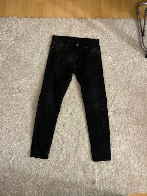 Svarta Levi's 512 jeans W30 L32 - Svarta jeans från Levi's modell 512 med klassisk femficksdesign och smal passform. Jeansen har en snygg mörk tvätt, knappgylf och Levi's ikoniska röda etikett på bakfickan. Perfekt för dig som gillar stilrena och tidlösa jeans.