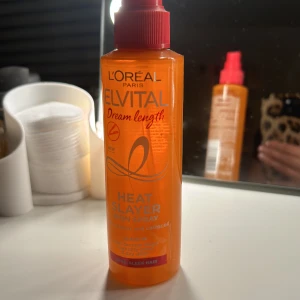 L'Oréal Elvital Dream Length Heat Slayer - Säljer en orange sprayflaska med röd pump från L'Oréal Paris Elvital Dream Length Heat Slayer Iron Spray. Produkten innehåller vitamin och ricinolja, och är en leave-in spray som skyddar håret mot värme och ger ett slätt resultat. Perfekt för dig som vill ha långt och glansigt hår.