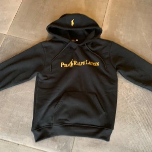 Polo Ralph lauren hoodie  - Svart hoodie från Polo Ralph Lauren med gul broderad logga på bröstet och huvan. Tröjan har snörning vid huvan, stor magficka och ribbade muddar. Perfekt för chill dagar och streetwear. Materialet är mjuk bomull och polyesterblandning. Klassisk och stilren look. Skick 8/10 modellen är 180cm och väger 73kg
