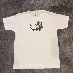 Vit t-shirt med grafiskt tryck - Säljer en vit t-shirt med Y2K tryck. T-shirten har rund hals och korta ärmar. Materialet är 100% bomull vilket gör den skön och lätt att bära. Tröjan är helt ny utan defekter och har aldrig använts. Tveka inte att skriva om du undrar något!