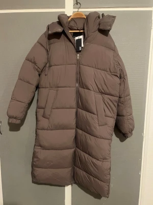 lång pufferjacka från 157 - Säljer en brun lång pufferjacka från Lager 157 med huva och dragkedja framtill. Jackan har två sidofickor, quiltad design. Perfekt för kalla dagar och har en clean look som funkar till många stilar. Den har en öppning på höger och vänster sida nertill som ger dig en frihet att röra benen. Storleken är loose fit. Priset är 600kr men kan diskuteras vid intresse. Fraktas samma dag med instabox, kan ge numret för extra säkerhet eller om man vill returnera? För mer bilder eller information skriv!❄️🧥
