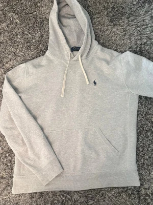 Riktigt najs grå Ralph lauren hoodie 🙌🤩 - Säljer en riktigt najs hoodie från Ralph lauren i storlek S. Finns en defekt som visas vid bild tre. Men ingenting som syns vid användning och är enkel att vika in🙌🤩