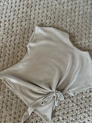 Beige knytblus från Zara - Säljer en beige blus från Zara med korta ärmar och snygg knytning i sidan. Toppen är tillverkad i ett mjukt stickat material och har en enkel, stilren design med rund hals. Perfekt för dig som gillar neutrala färger och bekväma plagg.
