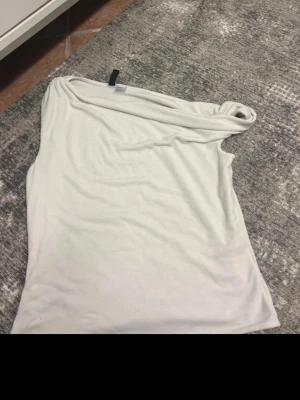 Vit oneshoulder topp - Säljer en stilren vit topp med oneshoulder-design. Toppen är ärmlös och har en mjuk, slät yta som ger en clean look. Perfekt för dig som gillar minimalistisk stil och vill ha något enkelt men snyggt i garderoben.