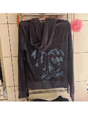 Juicy Couture❤️ - Säljer en mörkgrå hoodie från Juicy Couture i mjuk velour med strassdetaljer på ryggen och logga. Tröjan har huva, dragkedja med J-formad zip och två fickor fram. Perfekt för dig som gillar ikoniska 2000-tals vibes och comfy stil. Strl L på den men mindre i strl så passar super xs-m
