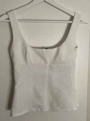 Vit topp från H&M - Säljer en stilren vit topp från H&M i storlek XS. Toppen har breda axelband, fyrkantig ringning och figurnära passform. Materialet är mjukt och lätt, perfekt för sommarens alla tillfällen. 