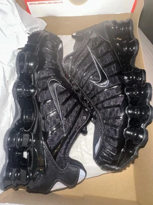 Nike Vapormax svarta sneakers - Nike Vapormax sneakers i helsvart färg med en chunky, transparent sula och snygga detaljer på ovandelen. Skorna har snörning och en sportig design med mesh och syntetmaterial. Perfekta för dig som gillar streetstyle och vill ha något som sticker ut.