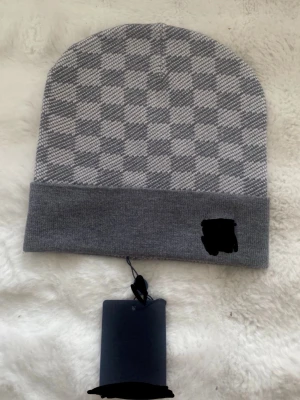 Grå rutig mössa med uppvikt kant - Snygg grå mössa med klassiskt rutigt mönster och bred uppvikt kant. Perfekt för att hålla värmen och samtidigt se stilren ut. Mössan har en neutral färgton som passar till det mesta och är tillverkad i mjukt material.