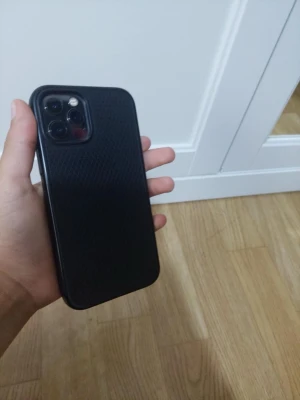 Smartphone med svart fodral - Smartphone med ett svart, mönstrat fodral. Skärmen ser hel ut och inga synliga sprickor eller större repor kan ses. Baksidan har ett skyddande skal. Perfekt för dig som söker en begagnad mobil i gott skick.