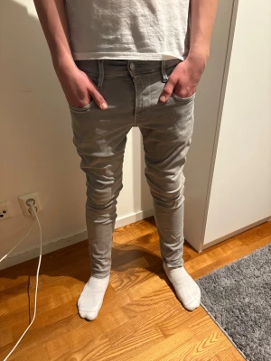 Grå slimfit jeans från Replay - Snygga grå jeans med skinny passform och klassisk femficksdesign. Byxorna har bälteshällor, knapp och dragkedja framtill samt raka bakfickor. Materialet är stretchigt och sitter tajt längs benen för en modern look.