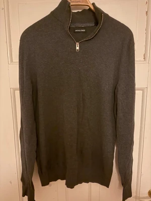 Grå half zip tröja från Jack & Jones - Snygg mörkgrå långärmad tröja från Jack & Jones med half zip i halsen. Tröjan har en hög krage och är tillverkad i mjukt material som känns skönt mot huden. Perfekt för dig som gillar stilrena och enkla plagg med en modern touch.