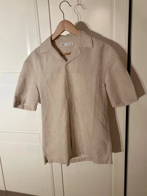 Beige kortärmad skjorta från Zara - Snygg beige kortärmad  skjorta från Zara i storlek S, tillverkad i en skön mix av linne och bomull. Perfekt för varma dagar och enkel att matcha med jeans eller shorts. Nypris: 300kr. Skriv vid minsta fundering🙌
