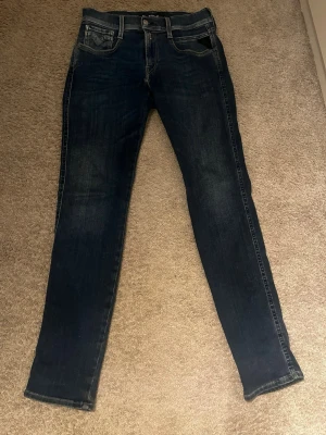 mörkblå replay  jeans slim fit - Säljer ett par snygga mörkblå jeans från Replay i slim fit-modell. Klassisk design med Replay-logga på fickan. Jeansen har normal midja och raka ben med lätt tvättad look. Perfekt för dig som gillar stilrena och moderna jeans.