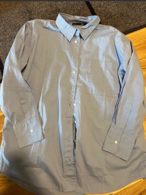 Ljusblå skjorta från 157 - Ljusblå skjorta från 157 i 100% bomull med klassisk krage, lång ärm och en stor bröstficka. Skjortan har knappar hela vägen framtill och är i en normal passform. Perfekt för dig som gillar enkel och clean stil Ljusblå skjorta med långa ärmar och en bröstficka. Skjortan har en klassisk krage och knäppning framtill.  Stor i storleken så tycker den är mer passande för en L varför jag väljer L som storlek :) aldrig använd! 