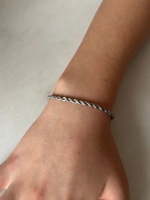 Tvinnat armband - Bilderna visar ett armband i silverfärgad metall med tvinnad kedja och karbinlås, nytt oanvänt. Ej äkta silver. 
