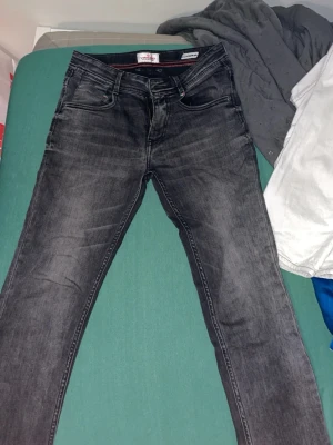 Svarta jeans från Vingino regular fit - Snygga svarta jeans från Vingino med regular fit och klassisk femficksdesign. Jeansen har en mörk tvätt med lätt slitna detaljer och kontrastsömmar i rött. Materialet är jeans och de har dragkedja och knapp framtill samt en liten italiensk flaggdetalj vid fickan.