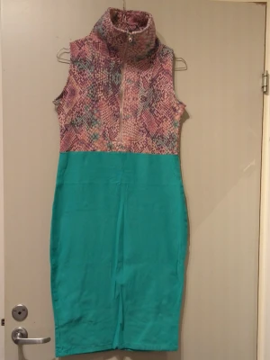 Grön  klänning med ormmönstrad topp - Säljer en ärmlös klänning med grön kjoldel och överdel i färgglatt ormmönster i rosa, lila och grönt. Klänningen har dragkedja framtill och rak passform som slutar vid knäna. Perfekt för dig som vill sticka ut med coola färger och mönster.