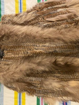 Brun pälsväst från Hollies Stockholm - Säljer en fluffig och lyxig brun pälsväst från Hollies Stockholm i storlek M. Västen är gjord av kaninpäls och har en naturlig mix av beige och bruna toner med snygga detaljer i pälsen. Perfekt för dig som vill ha en statement piece i garderoben.