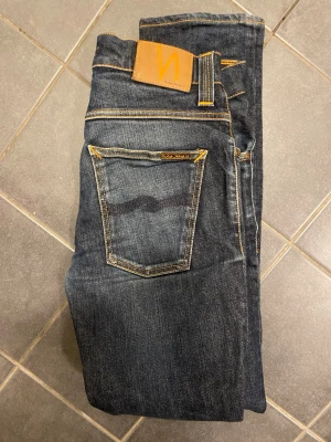 Nudie Jeans Grim Tim dry navy jeans - Snygga Nudie Jeans Grim Tim i färgen dry navy. Jeansen har klassisk femficksdesign, kontrastsömmar och är gjorda av 99% ekologisk bomull och 1% elastan. Passformen är rak och de har en stilren look med mörkblå ton.