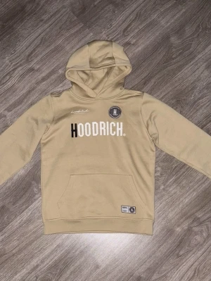 Hoodrich Hoodie - beige Hoodrich hoodie med huva och magficka. Hoodrich märket finns på både fram och baksidan. Hoodien har samt en bekväm passform.