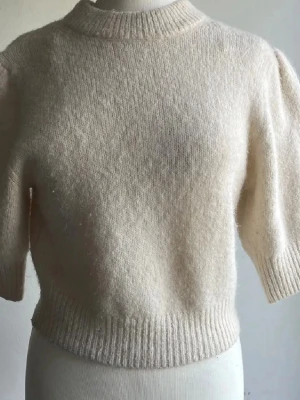 Vit stickad tröja med kort ärm & Other Stories  - Säljer en mjuk och mysig vit stickad tröja med korta ärmar och rund hals. Tröjan har ribbade muddar vid hals, ärmslut och nederkant. Perfekt för lager-på-lager och passar till både jeans och kjol.